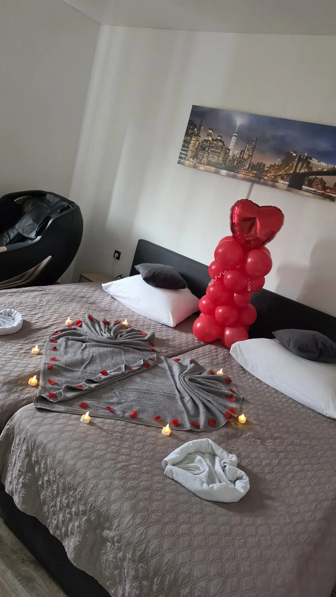 Doppelbett mit Handtuchherz, Rosenblättern, Kerzen und roter Ballonsäule